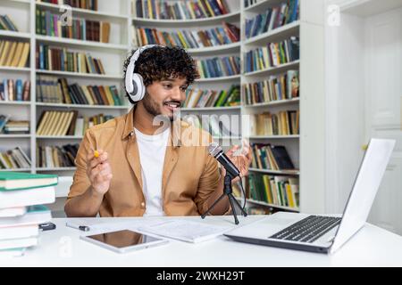 Ein leidenschaftlicher Schüler, der in die Aufnahme einer Podcast-Sitzung eingetaucht ist, umgeben von Büchern in einer Bibliothek, die eine Atmosphäre von Wissen und Technologie vermittelt. Stockfoto