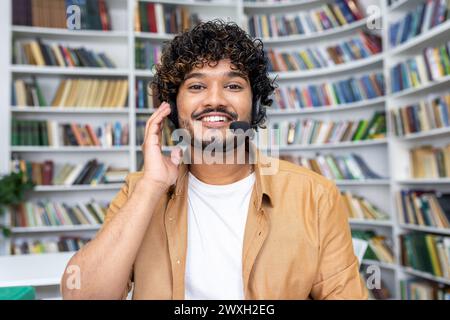 Ein fröhlicher junger Mann, der ein Headset trägt und lächelt, während er in die Kamera schaut, wahrscheinlich an einem Videoanruf teilnimmt oder als Student in einer virtuellen Klasse teilnimmt. Stockfoto