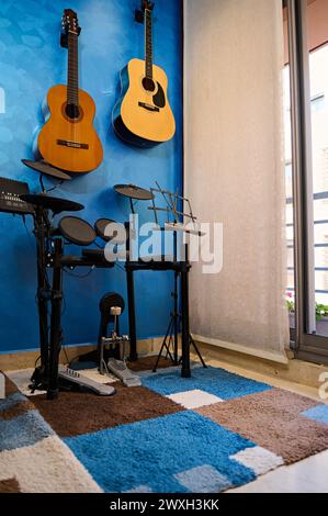 Moderne Innenausstattung eines Musikstudios für den Heimgebrauch. Akustische und elektrische Gitarren hängen an blauer Wand und Schlagzeug-Set. Hobbys und Freizeit. Musiker Stockfoto