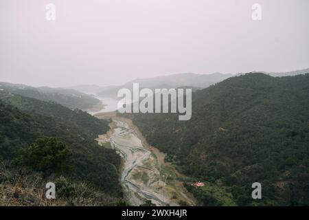 Marbella Istan Reservoir, Eine ruhige Szene eines sich windenden Flusses, der durch ein üppiges Tal fließt, mit Nebel bedeckt die fernen Hügel und einem einsamen Ort Stockfoto