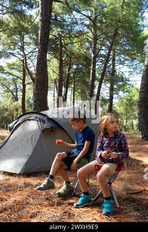 Zwei Kinder essen im Wald neben ihrem Zelt Stockfoto