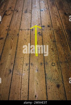Gelber Pfeil auf Holzboden, der nach vorne zeigt Stockfoto