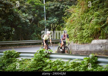 Zwei junge asiatische Radfahrerinnen, die auf der Landstraße Fahrrad fahren Stockfoto