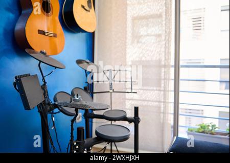 Moderne Einrichtung eines Musikstudios für Teenager-Musiker. Akustik- und E-Gitarren hängen an der blauen Wand und Schlagzeug mit schwarzen Zimbeln. Musikerr Stockfoto