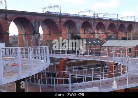 Stockport England Großbritannien 24. März 2024 Stockport City Centre neuer Verkehrsknotenpunkt. Die Konstruktion verfügt über eine auffällige Spiralrampe, die einen stufenlosen Zugang ermöglicht im Hintergrund befindet sich das Stockport Railway Viaduct mit einem Cross Country-Zug, der über den im März 2024 für die Öffentlichkeit eröffneten Autobahnkreuz fährt ©GED Noonan/Alamy Stockfoto