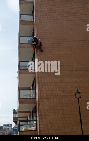 Vauxhall, London, Großbritannien. März 2024. Ein Bauunternehmer mit einem Kopf für Höhen hängt an einem Wohnblock neben der Vauxhall-Brücke und führt Wartungsarbeiten durch. Kredit: Maureen McLean/Alamy Stockfoto