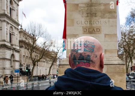Ein Mann mit Tätowierungen auf dem Kopf steht vor der Gedenkstätte Cenotaph in Whitehall in London. Ein Demonstrant ruft britische Militärveteranen ein Ende – die meisten Veteranen sind alte Menschen, und sie werden für die Strafverfolgungsmaßnahmen vor Jahrzehnten zur Verantwortung gezogen. Stockfoto