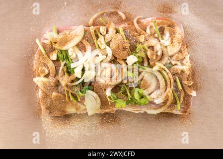 Blick von oben auf Fleisch mit Gewürzen, Zwiebeln und Knoblauchstücken, bereit zum Backen. Das Fleisch kochen. Stockfoto