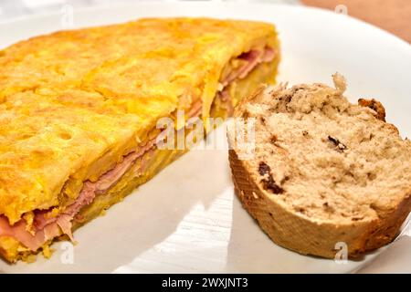 Spanisches Omelette mit Schinken und einer Scheibe nussigem Vollkornbrot auf einem Teller. Selektiver Fokus. Stockfoto