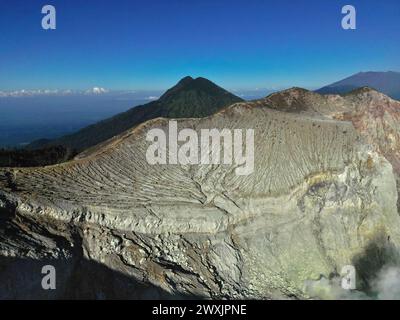 Atemberaubende Berglandschaft des Ijen-Vulkans mit einem Kraterfelsen, üppiger Vegetation, einem Tal und einem klaren blauen Himmel. Stockfoto