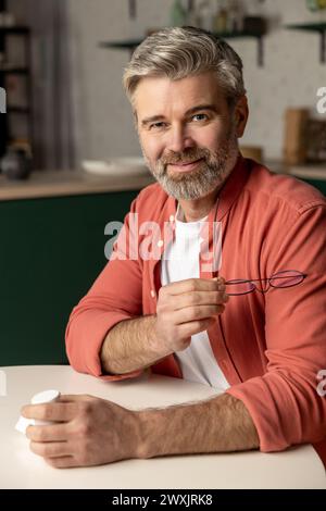 Lächelnder Mann mit orangefarbenem Hemd, der zu Hause am Tisch sitzt Stockfoto