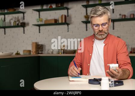 Diabetiker, der den Blutzuckerspiegel mit einem Glukometer überprüft, macht Notizen mit Indikatoren im Notizblock Stockfoto