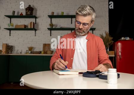 Diabetiker, der den Blutzuckerspiegel mit einem Glukometer überprüft, macht Notizen mit Indikatoren im Notizblock Stockfoto