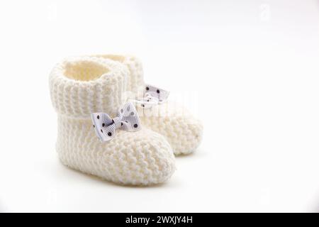 Weiße gehäkelte Babyschühchen mit schwarzen Punktschleifen auf weißem Hintergrund. Handgemachte Babyschuhe. Foto in hoher Qualität Stockfoto