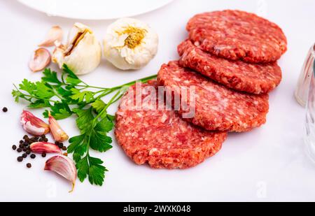 Rohes Rinderfleisch, Steak, Burger, Schnitzel auf weißem Teller, in der Nähe von Knoblauch, Pfeffer und Petersilie in einem Restaurant Stockfoto