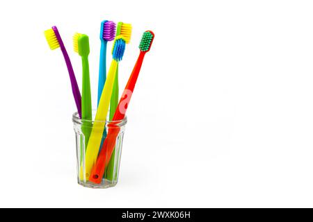Drei Zahnbürsten – violett, orange und gelb mit verschiedenfarbigen Borsten in einem durchsichtigen Becher auf weißem Hintergrund. Isoliert. Vertikal. Stockfoto