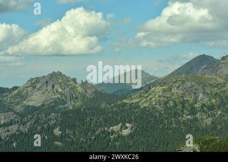 Eine riesige Bergkette mit spitzen Gipfeln, die von einem dichten Nadelwald unter einem bewölkten Himmel bewachsen sind. Berg „Burg“, Ergaki Naturpark, Krasnojarsk Stockfoto