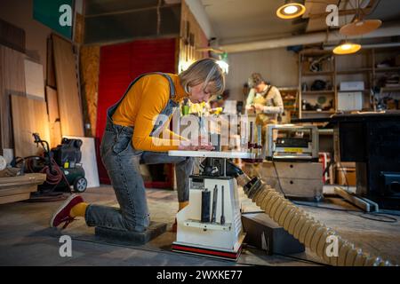 Die fokussierte Zimmerfrau arbeitet in der Tischlerei und dreht Holzgegenstände auf Drehmaschine. Tischlerei Stockfoto