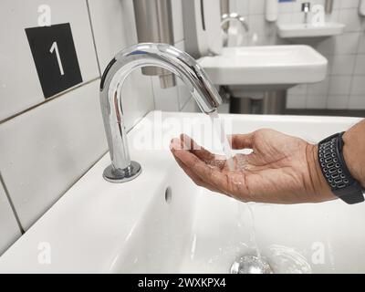 Nahaufnahme eines Mannes wäscht sich die Hände mit einem berührungslosen Wasserhahn. Stockfoto