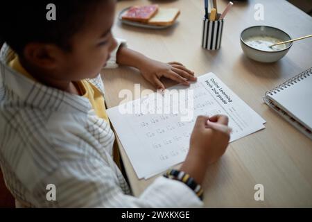 Blick über die Schulter auf den jungen afroamerikanischen Jungen, der Hausaufgaben am Küchentisch macht und mathematische Tests löst Stockfoto