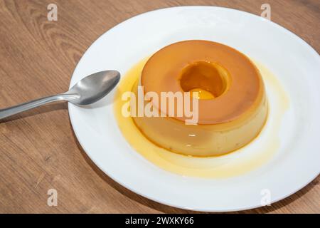 Ein Holztisch mit einem weißen Flan-Teller, der mit Sirup getränkt ist Stockfoto