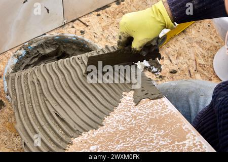 Fliesenleger verteilt Zementmörtel mit einer gekerbten Kelle auf die Fliesenoberfläche. Stockfoto
