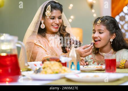 Glückliche indische Mutter Fütterung Dates zu Tochter während ramadan iftar Abendessen zu Hause - Konzept der fürsorglichen Mutter, ramazan Festival und gesunde Ernährung. Stockfoto