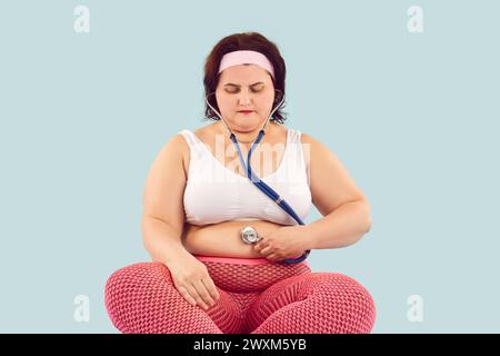 Fettleibige übergewichtige Frau hält ein Stethoskop an ihrem fetten Bauch und hört ihren Darmgeräuschen zu Stockfoto