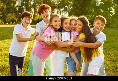 Fröhlich lächelnde Kinder stehen zusammen im Sommerpark in der Natur und umarmen sich im Freien. Stockfoto