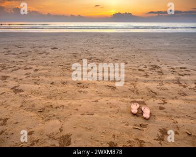 Pinke leere Flipflops mit niemandem am Sandstrand, friedliche Meereslandschaft im Paradies-Hintergrund am wunderschönen idyllischen Sonnenuntergangshimmel, im Sommer. Sommerreisen, HO Stockfoto