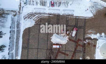 Drohnenfotografie des Traktors beim Schneeräumen des öffentlichen Platzes während des bewölkten Wintertages Stockfoto