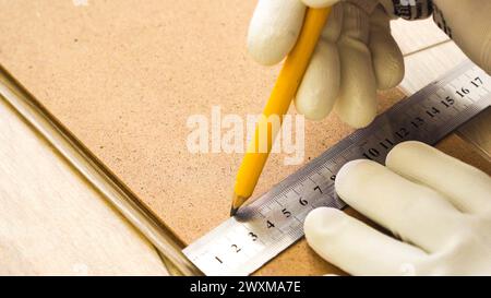 Nahaufnahme eines männlichen Bauarbeiters mit Metalllineal und Bleistift beim Zeichnen einer Linie auf Laminatfußboden. Stockfoto