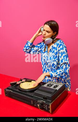 Junge, stilvolle Frau, dj, der Sound-Mixer mit Pfannkuchen anstelle von Schallplatten auf rosafarbenem Hintergrund verwendet. Poster mit kreativer Musik. Party Stockfoto