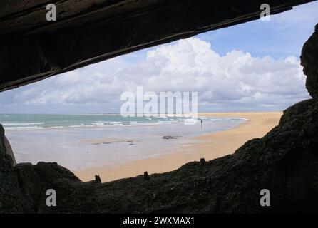 Blick auf die Küste vom Inneren eines bombardierten deutschen Bunkers aus dem Zweiten Weltkrieg am Strand von Erdeven, Bretagne. Ein Mann, der allein am Strand läuft. Sonniger Frühlingstag. Sel Stockfoto