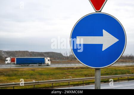Vorgeschriebenes Richtungspfeil auf der Autobahn mit zwei Lkw im Hintergrund, selektiver Fokus Stockfoto