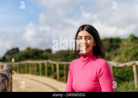 Porträt einer lächelnden jungen Frau mit rosa Pullover im Park Stockfoto