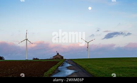 Windturbinen drehen sich in der Ferne, während der Mond über einer Landstraße untergeht Stockfoto