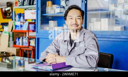 Ein Mann in einem blauen Hemd sitzt an einem Schreibtisch mit Handy Stockfoto