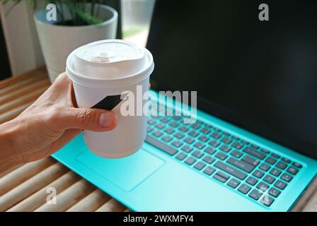 Hand hält eine Tasse Getränk mit Laptop im Hintergrund Stockfoto