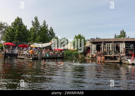 Die Gäste schwimmen und entspannen sich an einem Sommertag in einer lebhaften Bar am Wasser in Amsterdam Noord mit Sitzgelegenheiten im Freien und Musik am waldgesäumten Fluss Stockfoto