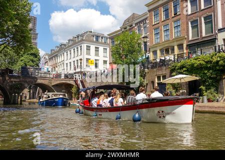 Touristenboot, das an einem sonnigen Tag in den Niederlanden entlang eines malerischen Kanals im Zentrum von Utrecht fährt, umgeben von historischen Gebäuden und Brücken Stockfoto