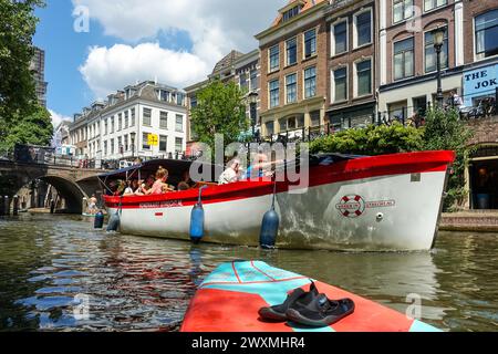 Touristenboot, das an einem sonnigen Tag in den Niederlanden entlang eines malerischen Kanals im Zentrum von Utrecht fährt, umgeben von historischen Gebäuden und Brücken Stockfoto