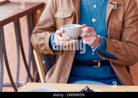 Frau in Blau mit blauer Maniküre hält eine Kaffeetasse mit Cappuccino. Stockfoto