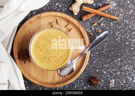 Indischer Masala Chai Tee. Masala Chai gewürzter Tee mit Milch und Gewürzen auf dunklem rostigem Hintergrund flach gelegt. Gemütliche häusliche Ästhetik. Stockfoto