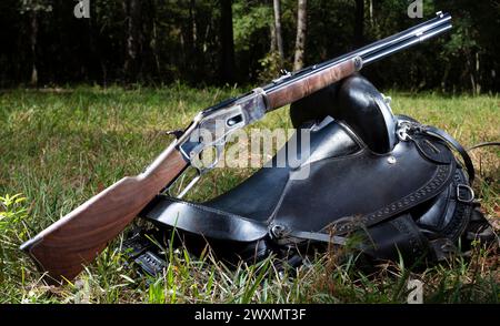 Ein Akkugewehr im Cowboy-Stil, das auf einem Sattel in einem grünen Wald ruht. Stockfoto