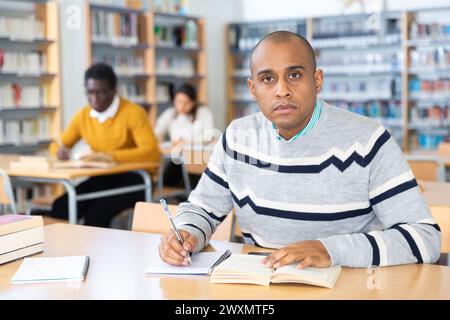 Junger erwachsener Mann, der in der öffentlichen Bibliothek studiert Stockfoto