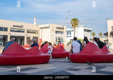 Tel Aviv, Israel - 6. Januar 2023: Menschen sitzen auf roten Bänken, an einem sonnigen Tag in einer Straße in Tel Aviv, Israel. Stockfoto