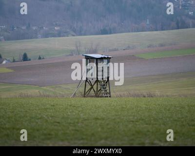 Jagdstand oder Hochsitz für Jäger in einer ländlichen Landschaft mit landwirtschaftlichen Feldern. Holzhütte, in der sich Menschen verstecken und auf Tiere schießen können. Stockfoto