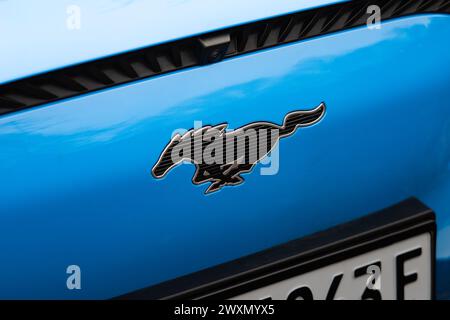 Ford Mustang Emblem auf der Vorderseite eines blauen Elektroautos. Logoschild mit dem Laufpferd als Teil der Automobilmarke. Stockfoto