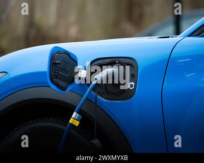 Laden Sie den Ford Mustang Mach-E mit dem Stecker in der Autobuchse in Nahaufnahme auf. Elektromobilität als Alternative. Das EV verwendet moderne Ladetechnologie. Stockfoto